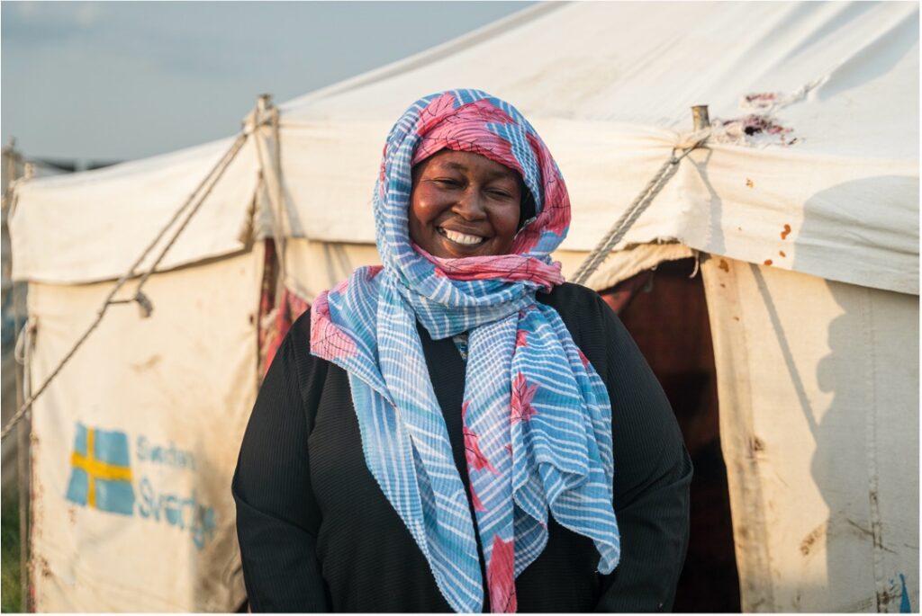 A Sudanese woman standing in front of a refugee camp