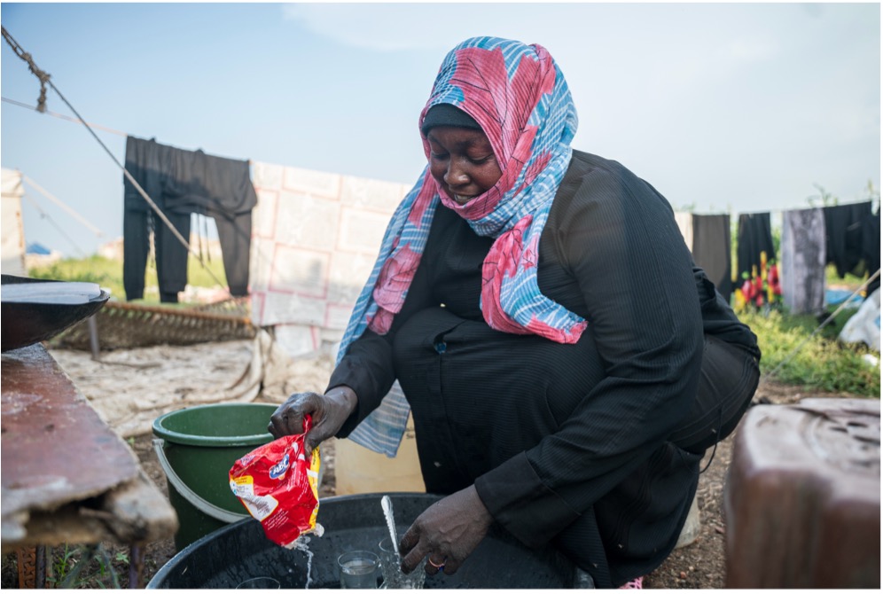 A Sudanese woman washing her cultery with limited clean water, a pressing challenge of displaced families in Sudan